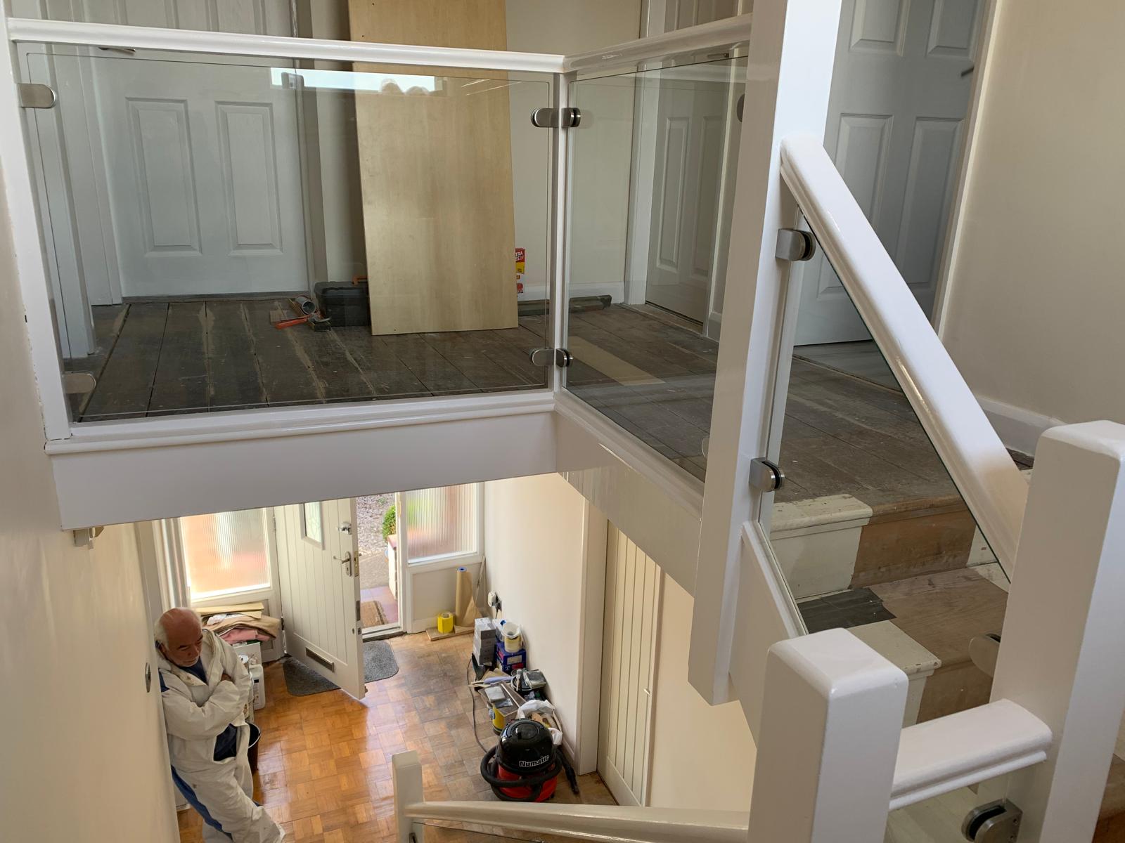 Stainless steel D-shaped clamps on TUFF CYMRU toughened glass balustrade on white-painted staircase